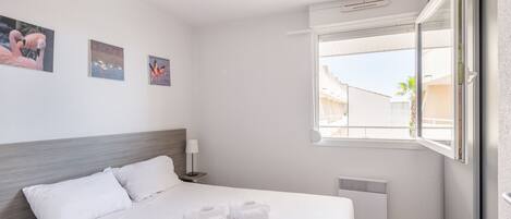Habitación de hotel con cama, ropa de cama blanca, mesita de noche con lámpara y decoración en la pared.