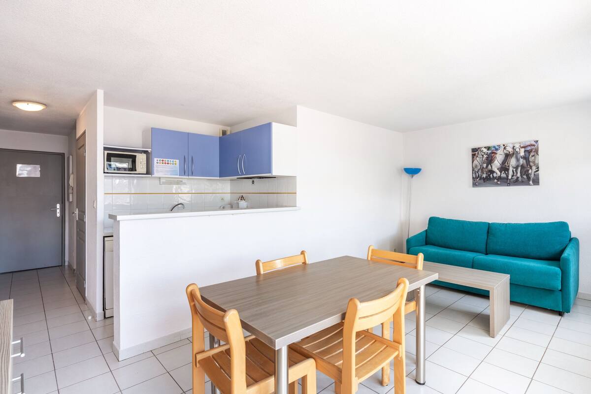 Un espace de vie compact comprenant une kitchenette, un coin repas et un canapé de couleur turquoise.