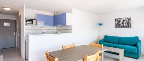Un espacio habitable compacto con kitchenette, comedor y un sofá color turquesa.