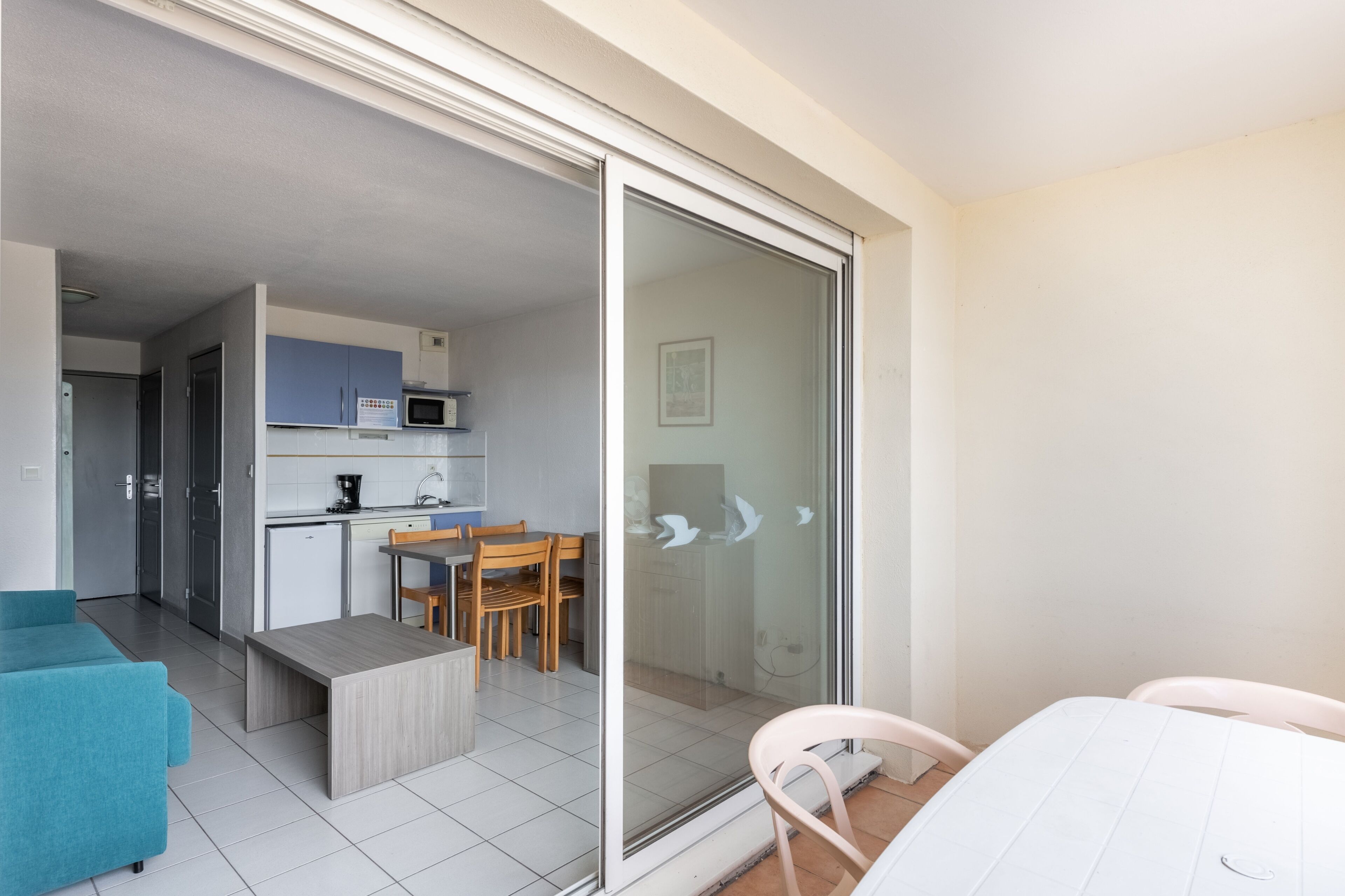 A modern apartment with a kitchen, dining area, and a balcony with a sliding glass door.