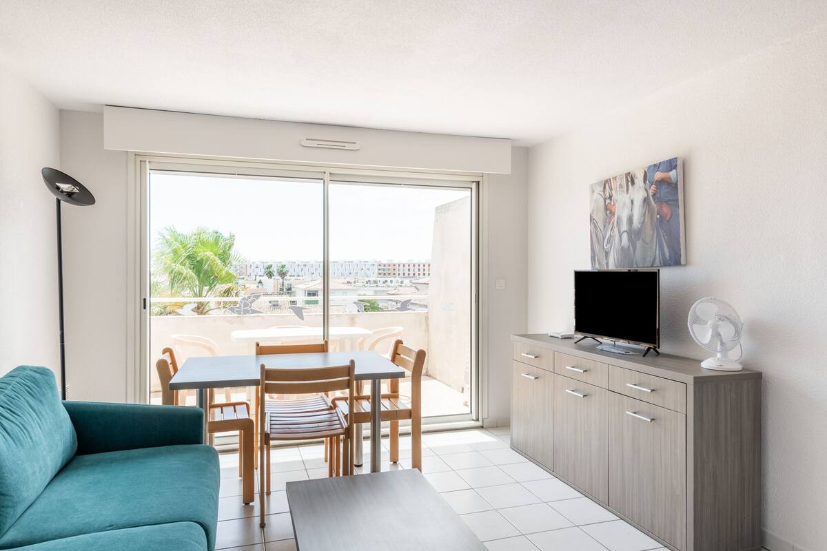 Un salon moderne comprenant un canapé, une table à manger avec des chaises, un téléviseur posé sur un meuble et un balcon offrant une vue sur la ville.