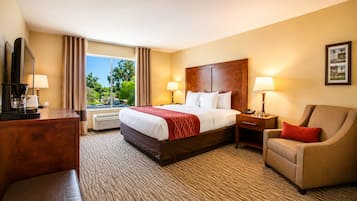 A hotel room with a bed, a desk, a chair, and a large window with curtains.