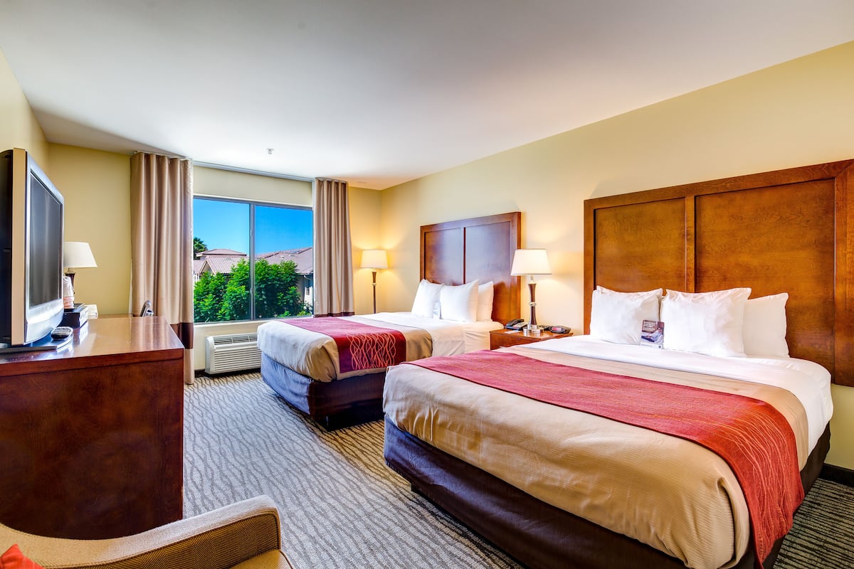 A hotel room with two beds, a desk, and a TV.