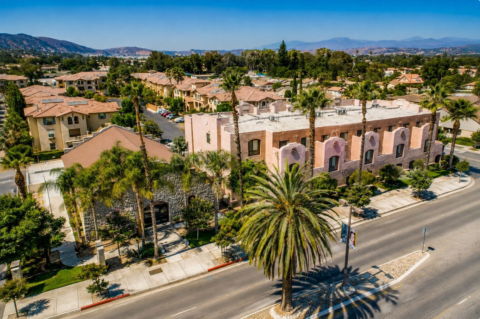 A residential area with multiple-story buildings, palm trees, and a clear sky.