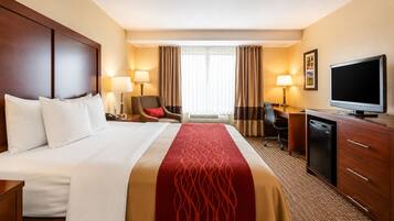 A hotel room with a large bed, a desk with a television, a chair, and a desk lamp.
