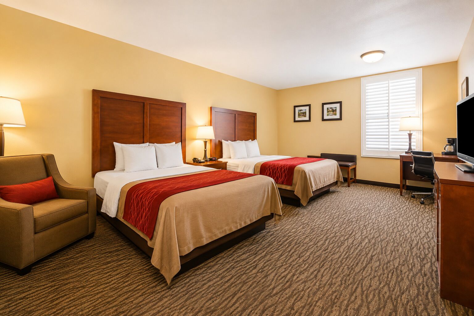 A hotel room with two beds, a desk, a chair, and a television.