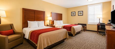 A hotel room with two beds, a desk, a chair, and a television.