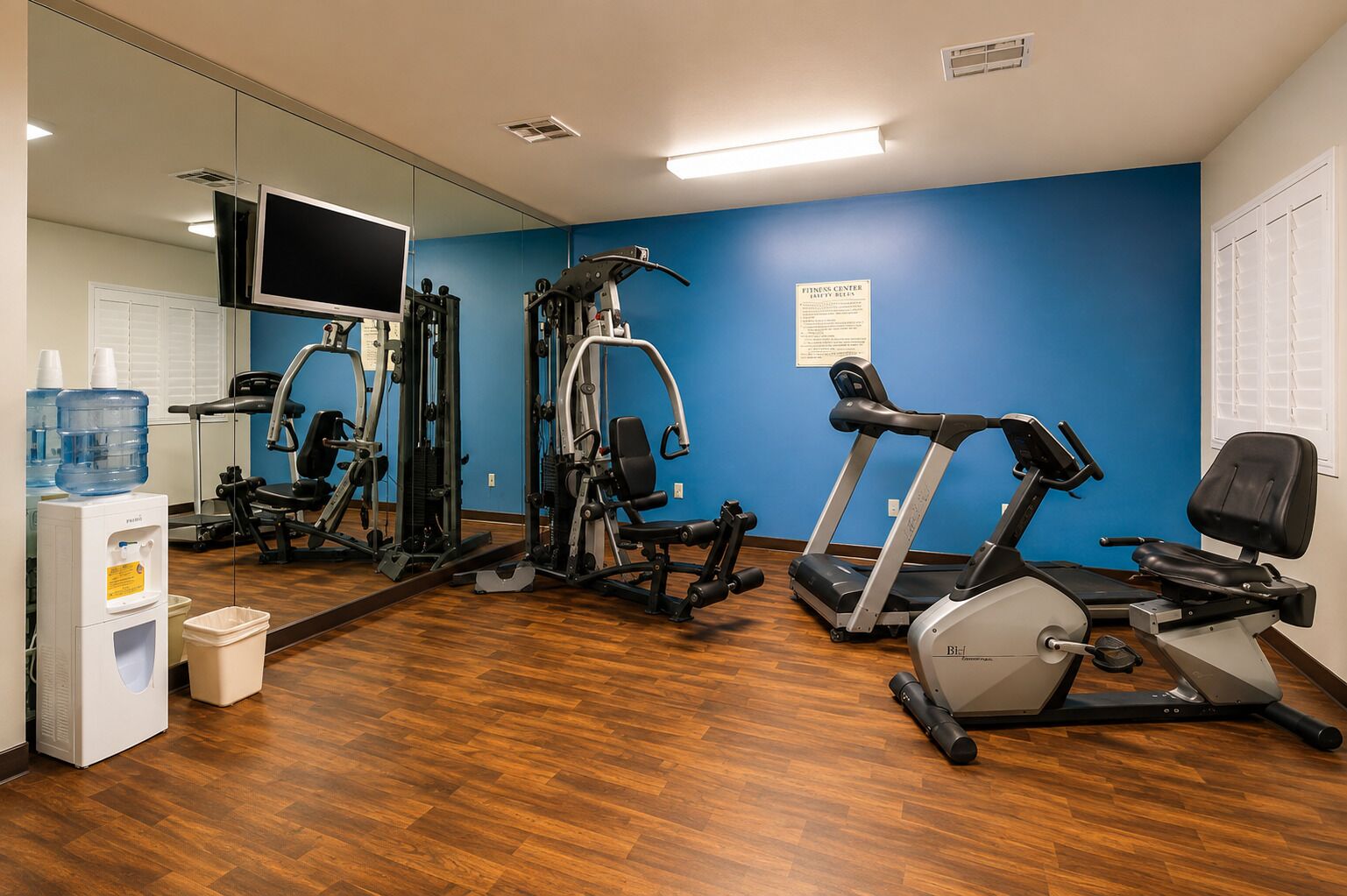Een fitnessruimte met trainingsapparatuur, een waterdispenser en een spiegel.
