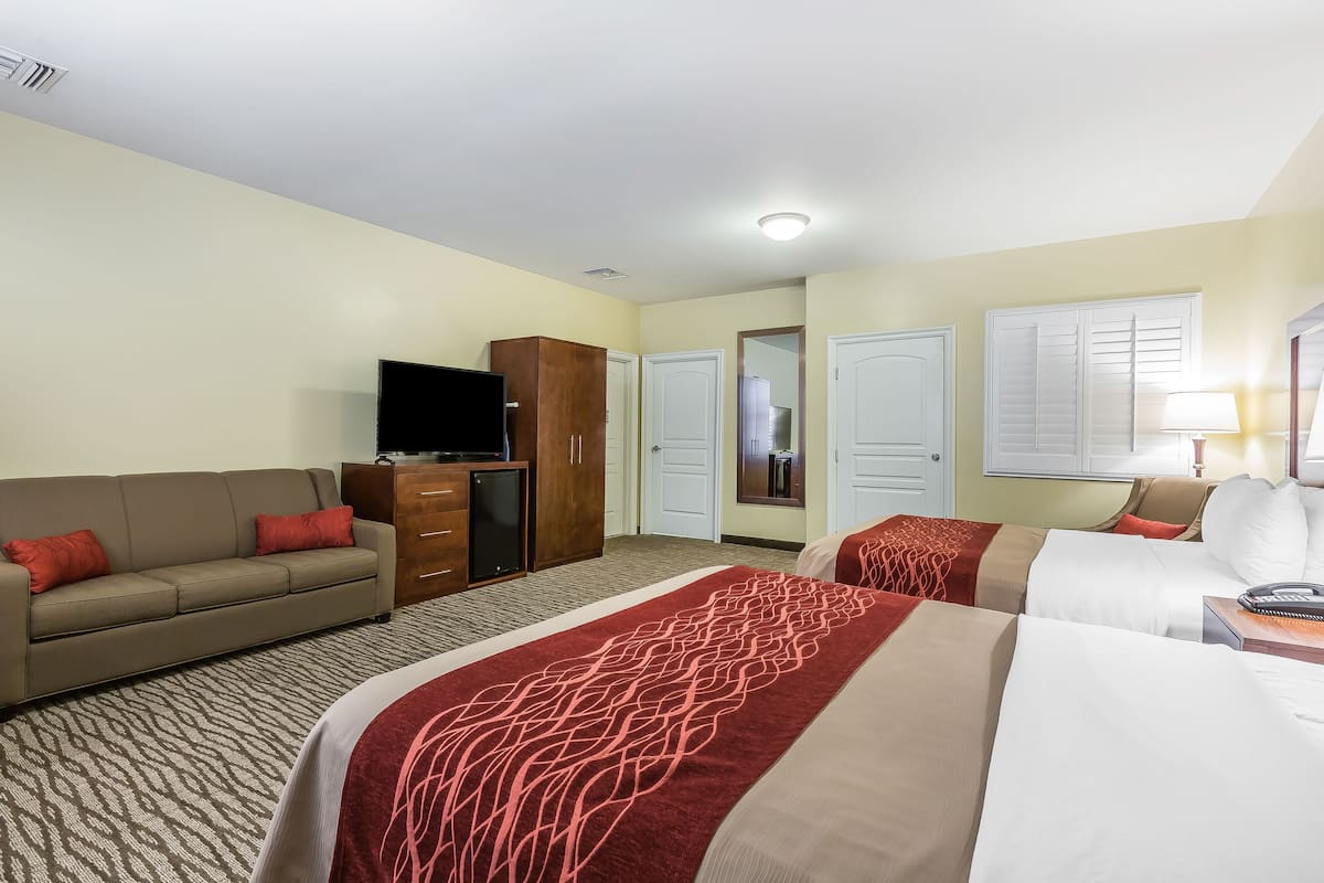 A hotel room with a bed, a sofa, a TV, a wardrobe, and a desk with a lamp.