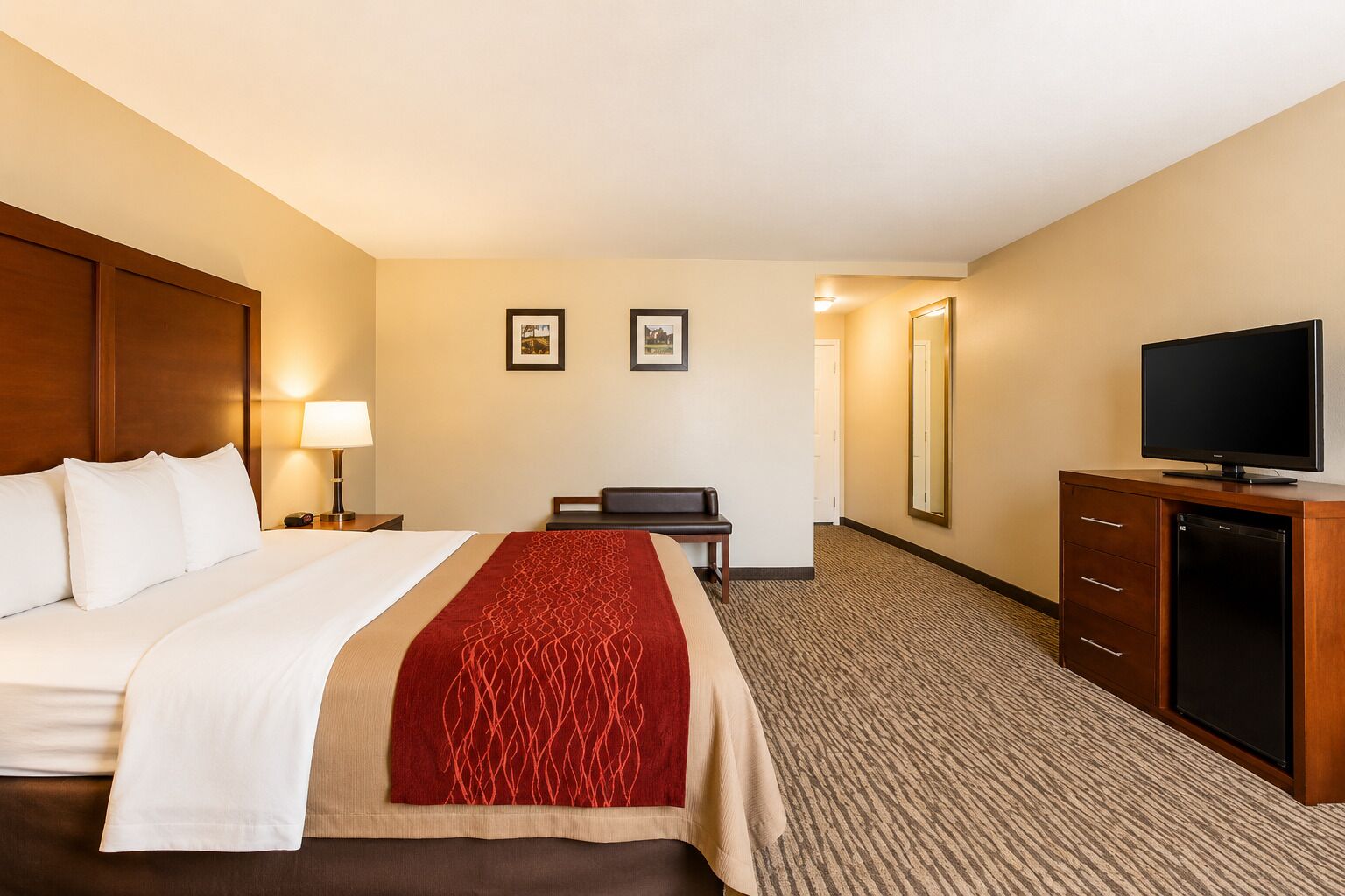 A hotel room with a bed, a desk, a television, and a mirror.