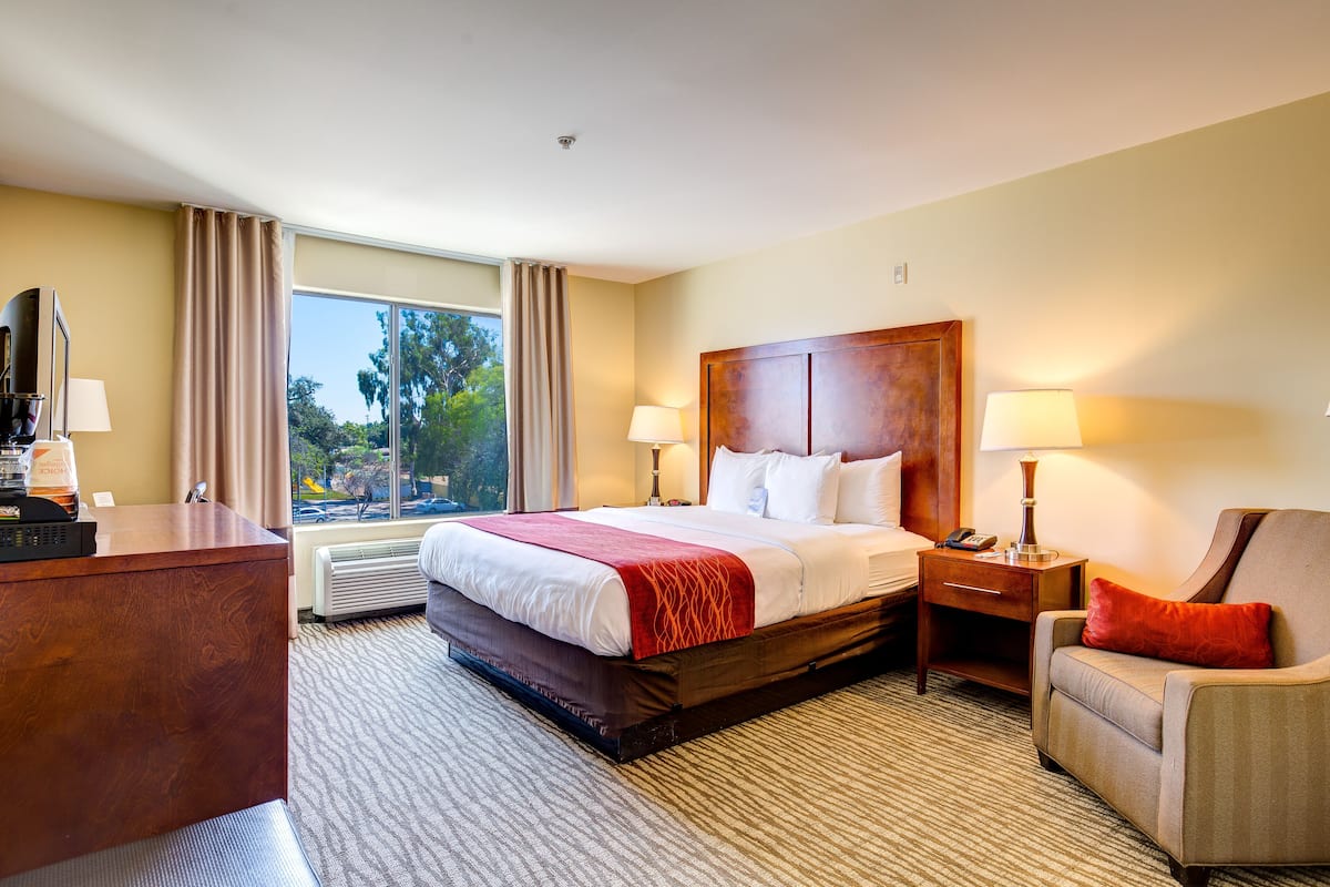 A hotel room with a large bed, a desk, a chair, and a window with curtains.