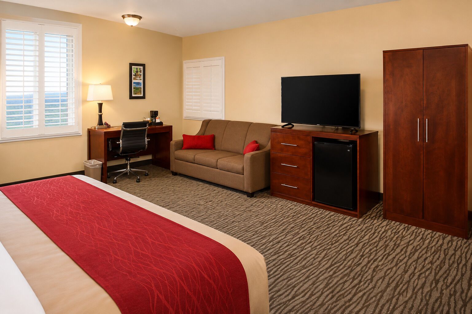 A hotel room with a bed, a desk, a sofa, a television, and a wardrobe.