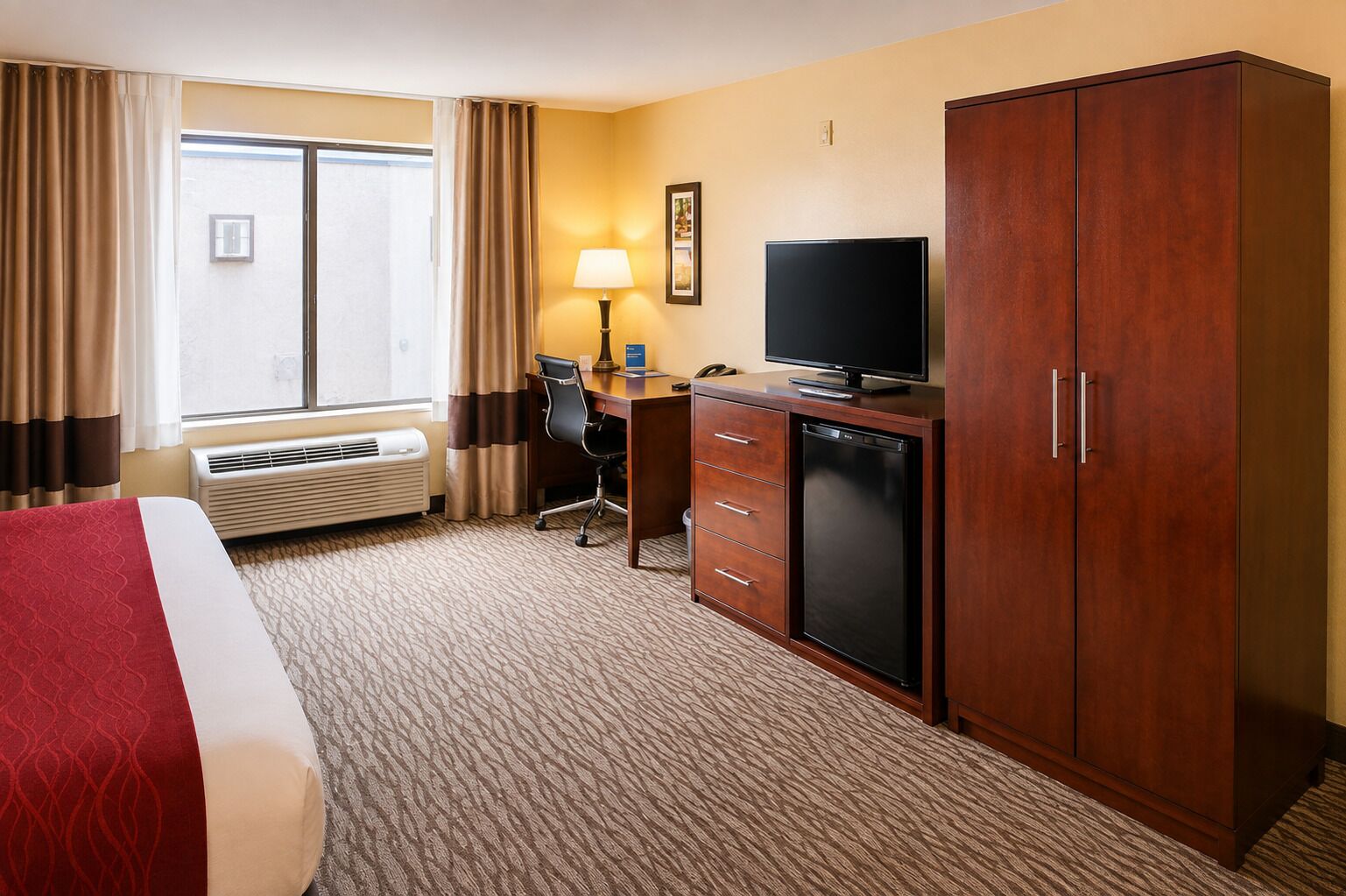 A hotel room with a bed, desk, television, wardrobe, and a window with curtains.