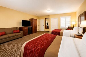 A hotel room with a sofa, two beds, a TV, a wardrobe, and a mirror.