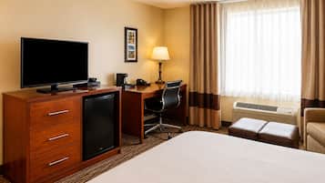 A hotel room with a bed, a desk with a computer, a television, a lamp, a chair, and a small refrigerator.