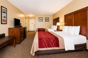 A hotel room with two beds, a desk, a television, and a door.