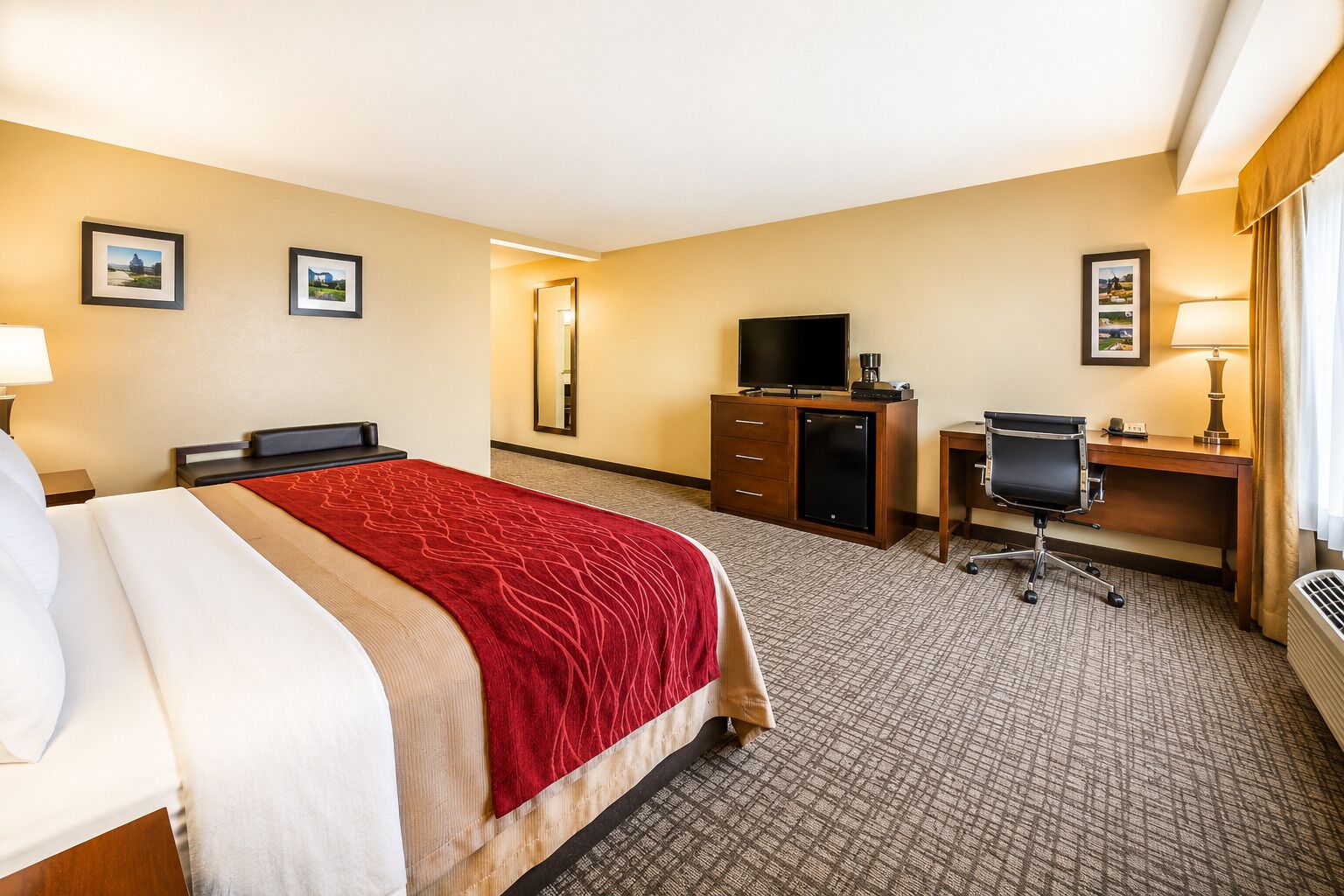 A hotel room with a bed, a desk, a chair, a television, and a minibar.