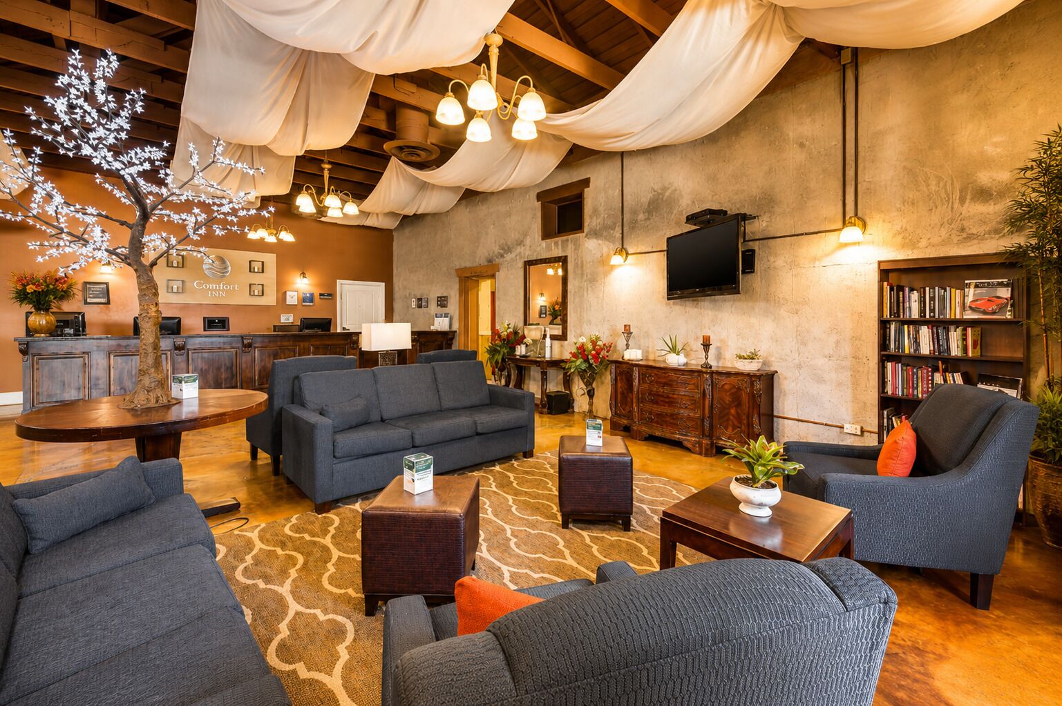 A hotel lobby with a reception desk, sofas, a coffee table, a bookshelf, and a large tree with lights.