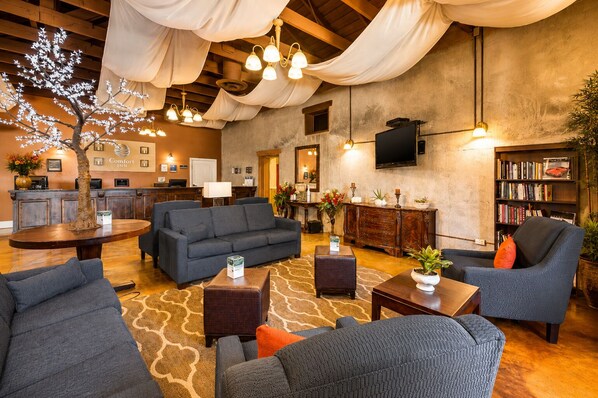 A hotel lobby with a reception desk, sofas, a coffee table, a bookshelf, and a large tree with lights.