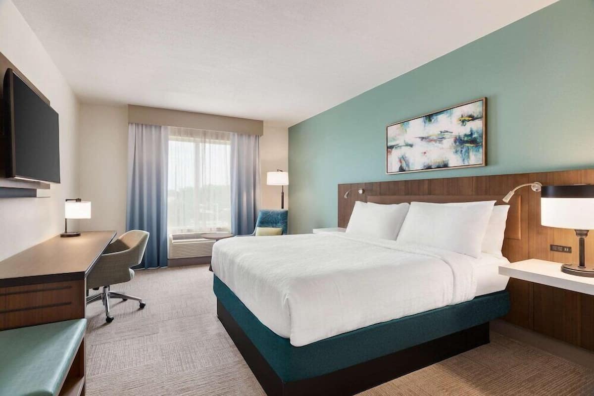 A hotel room with a bed, desk, chair, and a television.