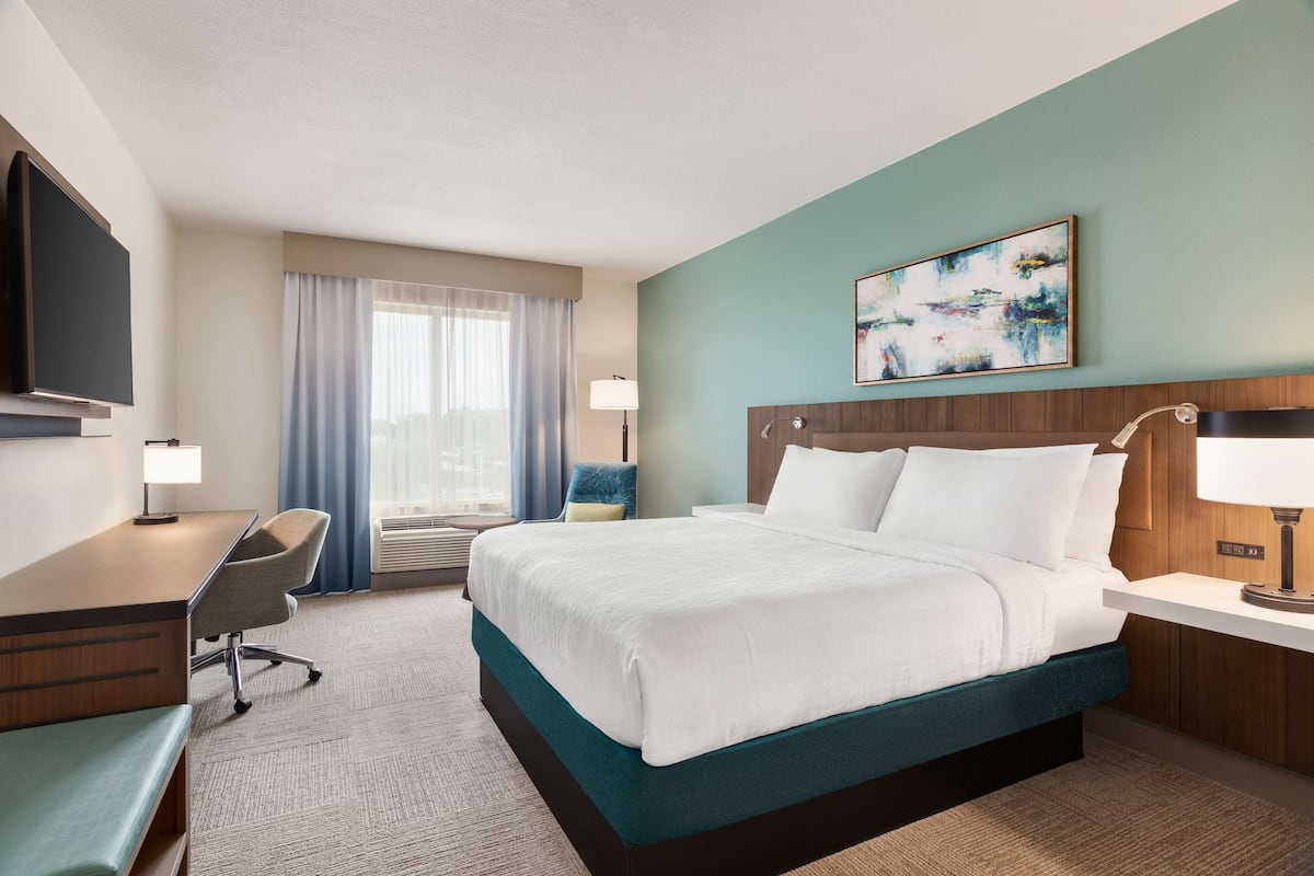 A hotel room with a bed, desk, chair, and a TV.