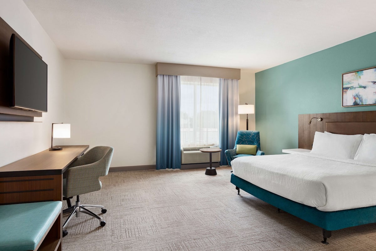 A hotel room with a bed, desk, chair, and a TV.