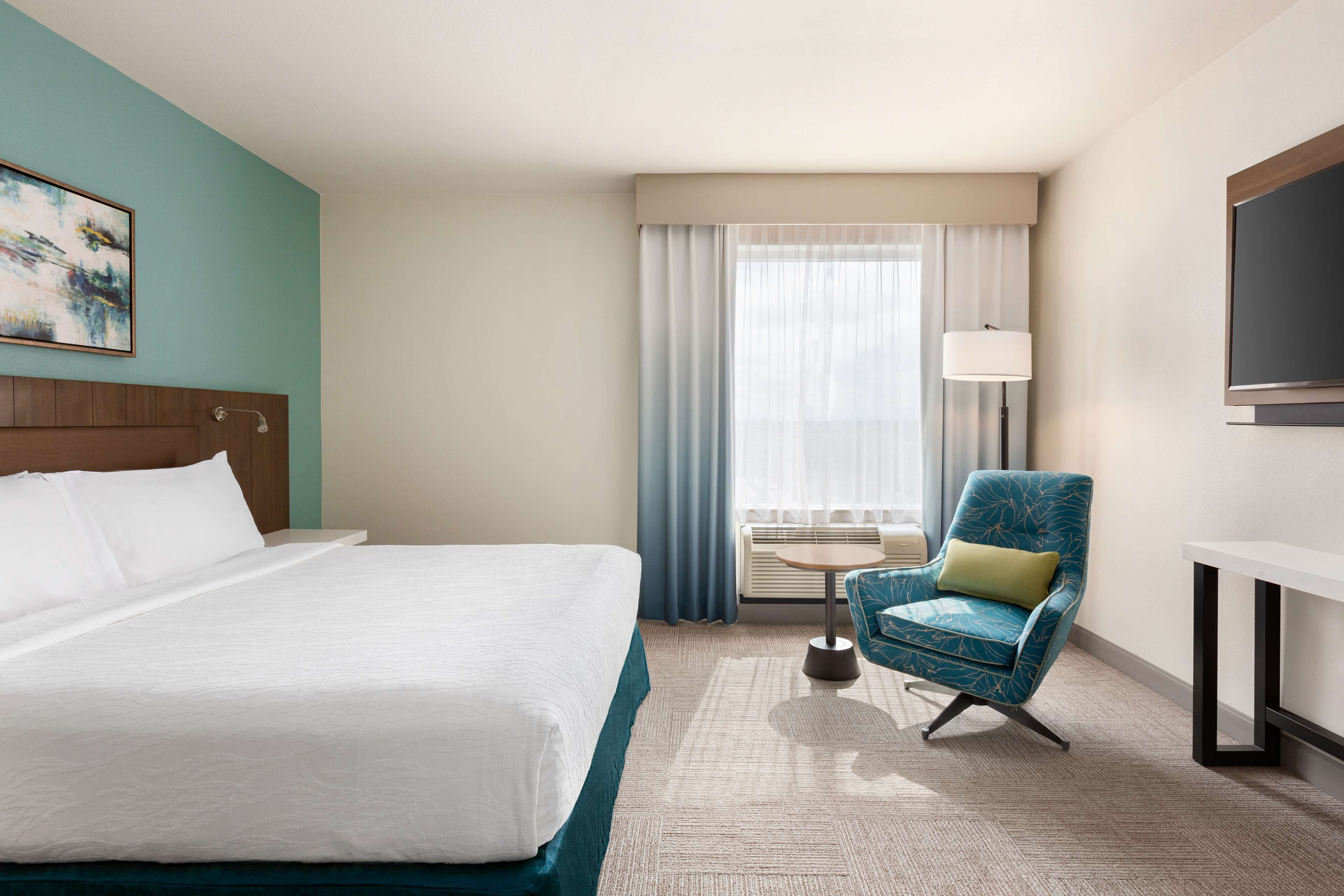 Una habitación de hotel con una cama grande, una silla, una mesita y un televisor.