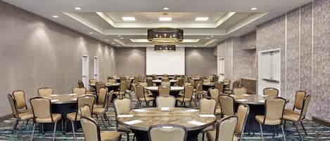 A conference room with multiple round tables and chairs, a large chandelier, and a patterned carpet.