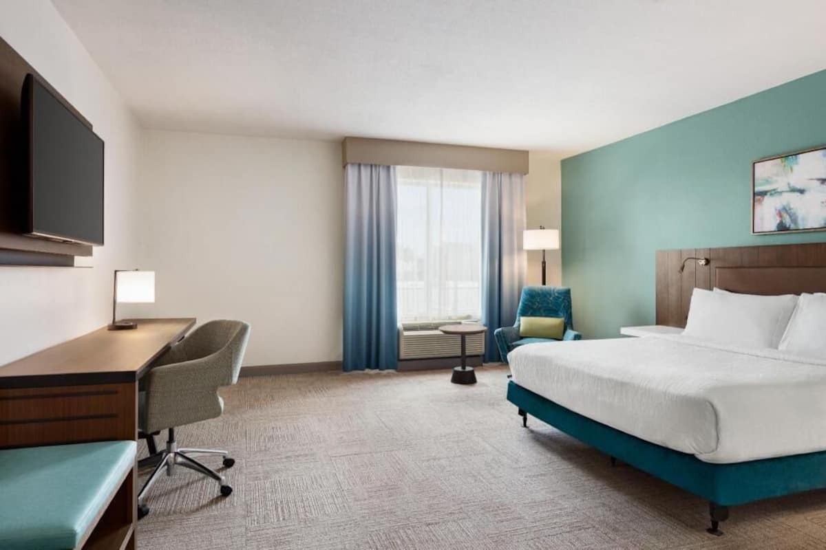 A hotel room with a bed, desk, chair, and a TV.