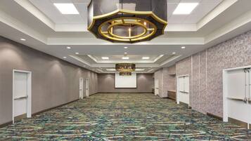 A spacious, carpeted hallway with a patterned floor, recessed lighting, and a large, ornate chandelier.
