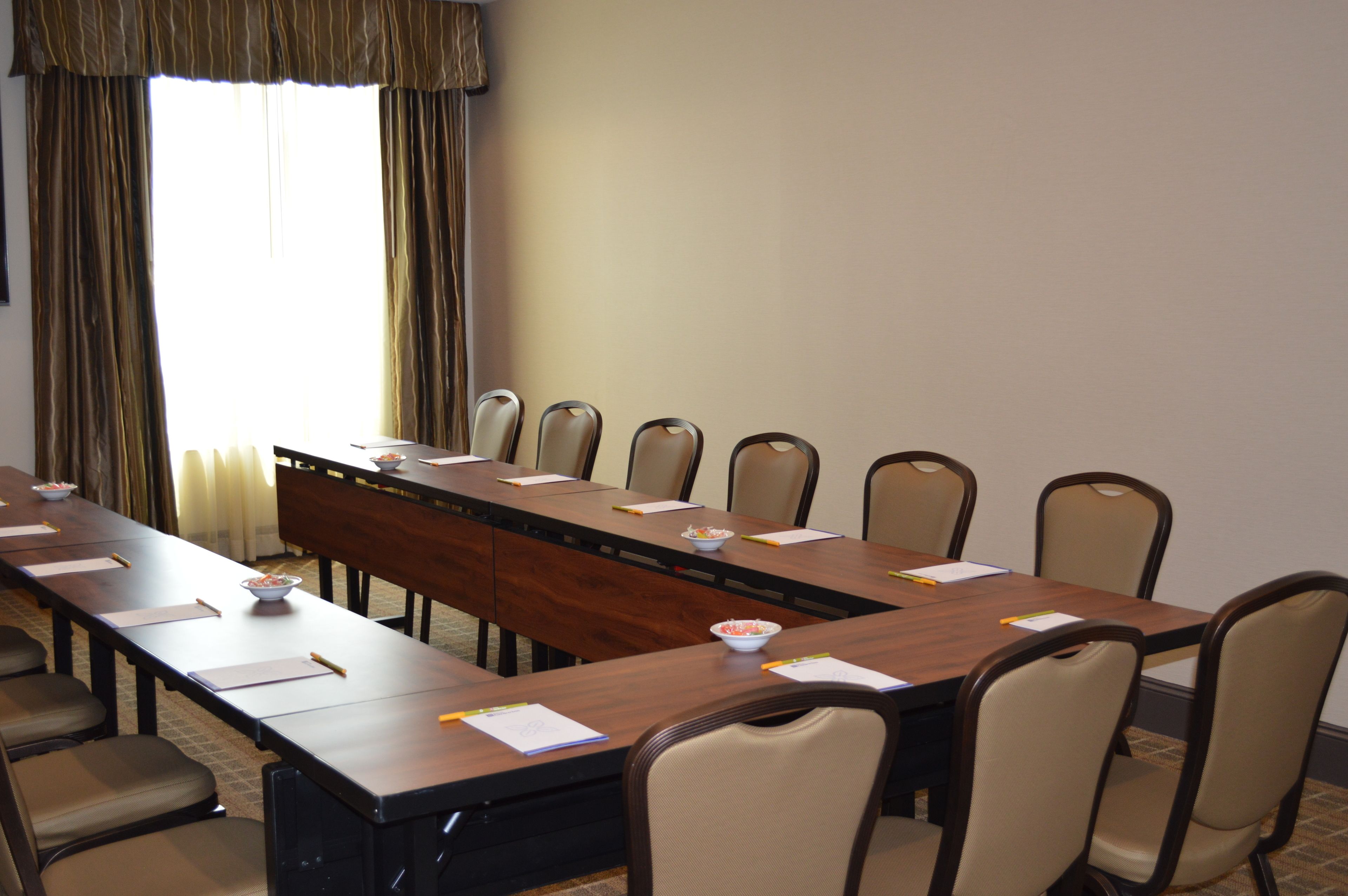 A conference room with a long table, chairs, and a window with curtains.