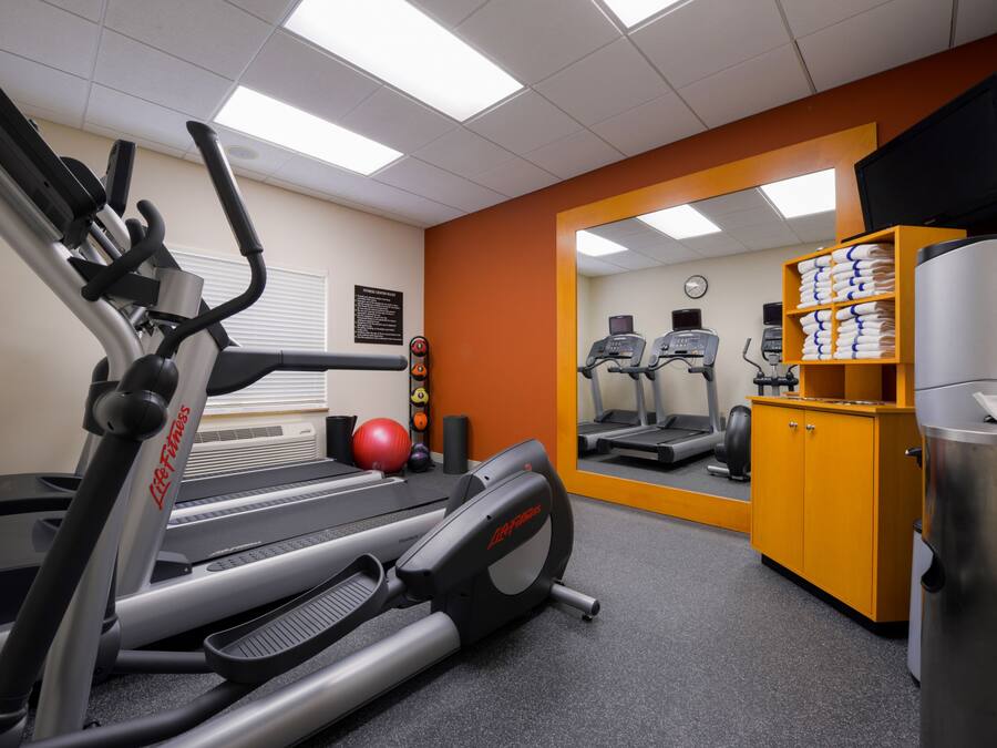 Un gimnasio con cintas de correr, una bicicleta estática y un espejo grande.