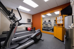 Un gimnasio con cintas de correr, una bicicleta estática y un espejo grande.