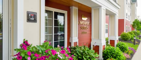 Entrada de un hotel con un cartel que dice "OMEWOOD SUITES" y un jardín bien cuidado con diversas flores.