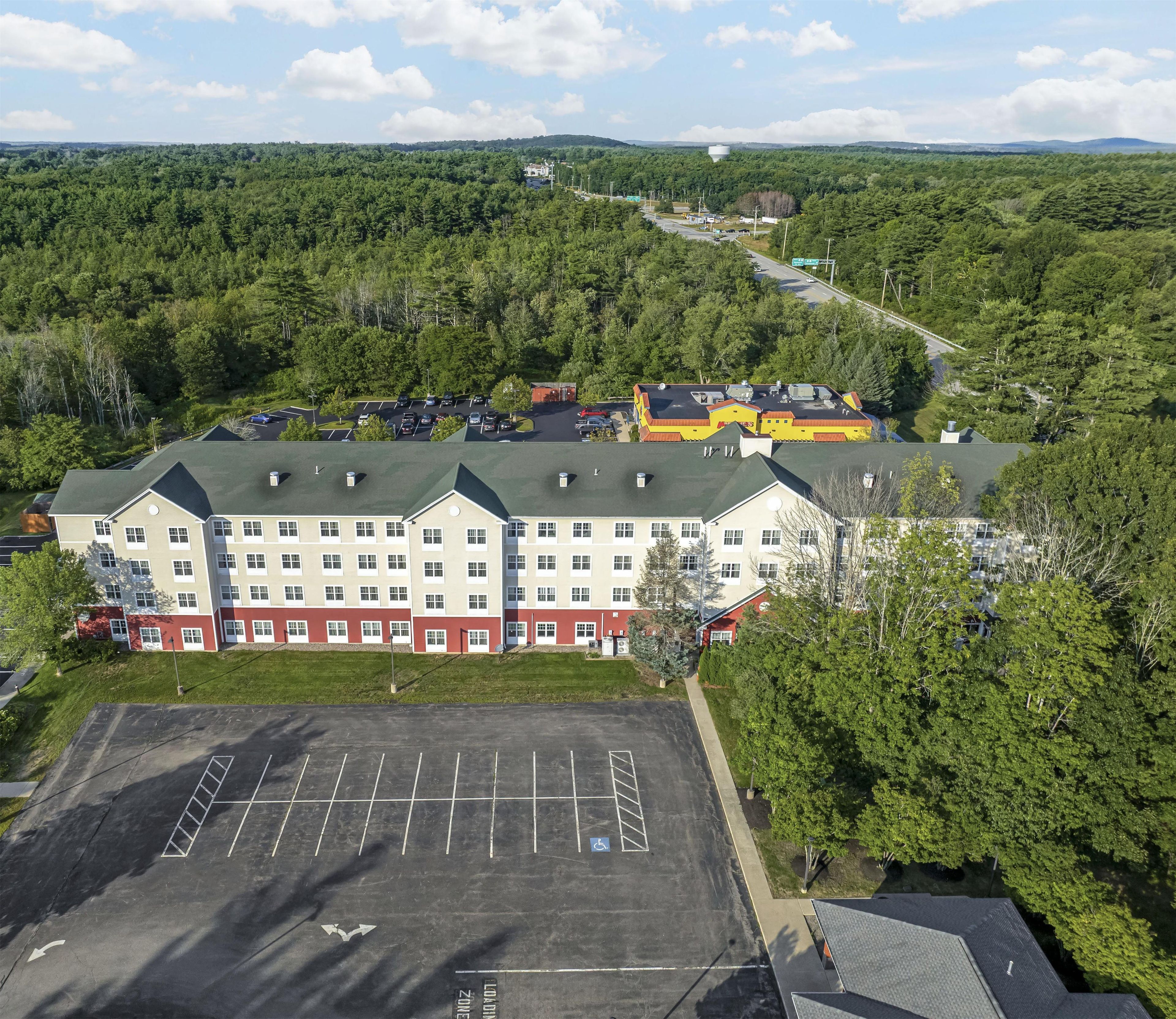 A multi-story hotel with a parking lot in front, surrounded by dense forest.