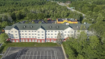 A multi-story hotel with a parking lot in front, surrounded by dense forest.