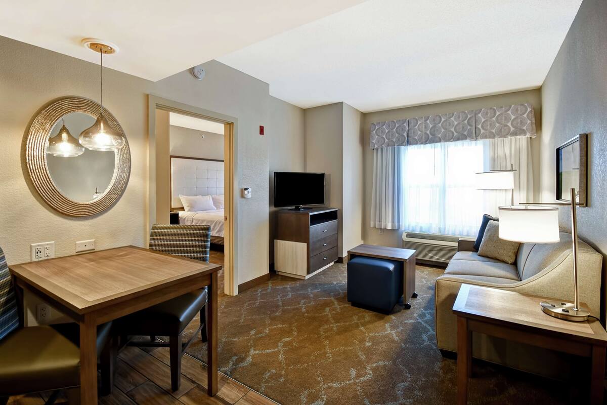 Een hotelkamer met een houten eettafel, een bank, een televisie en een lamp.