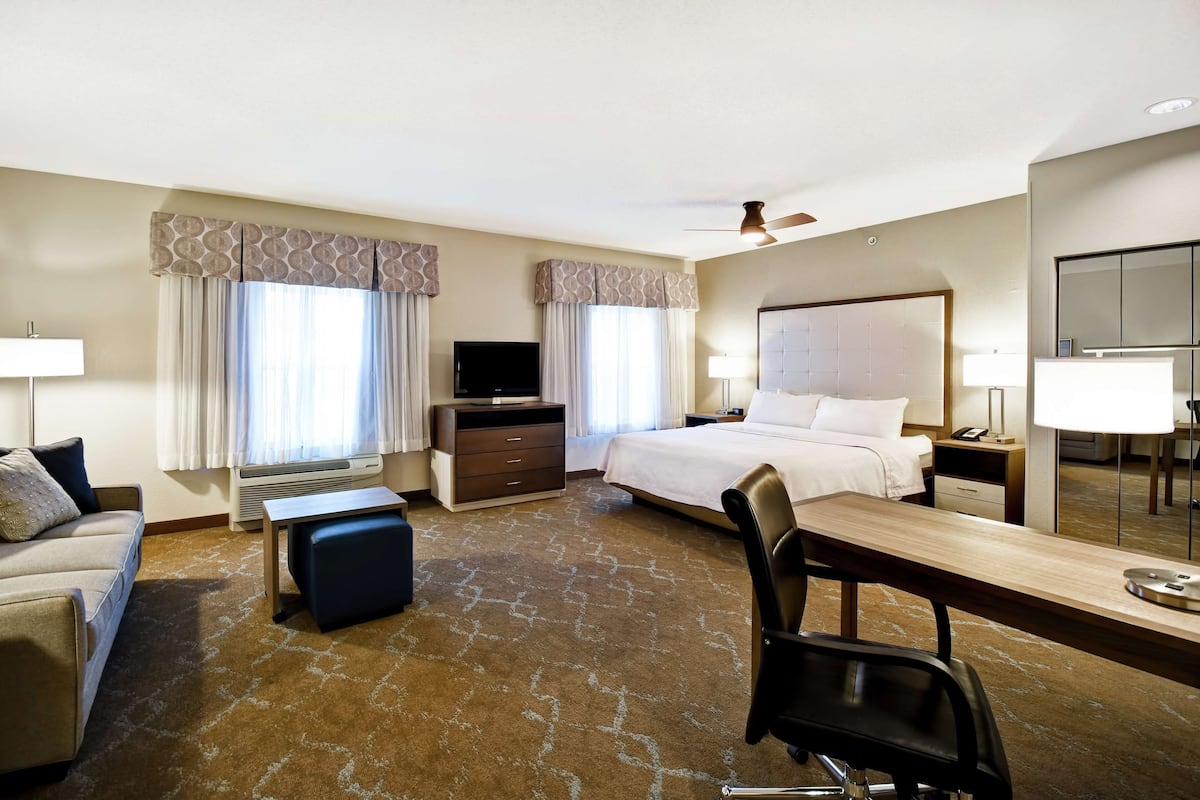 Een hotelkamer met een bed, bureau, stoel, televisie en een grote spiegel.