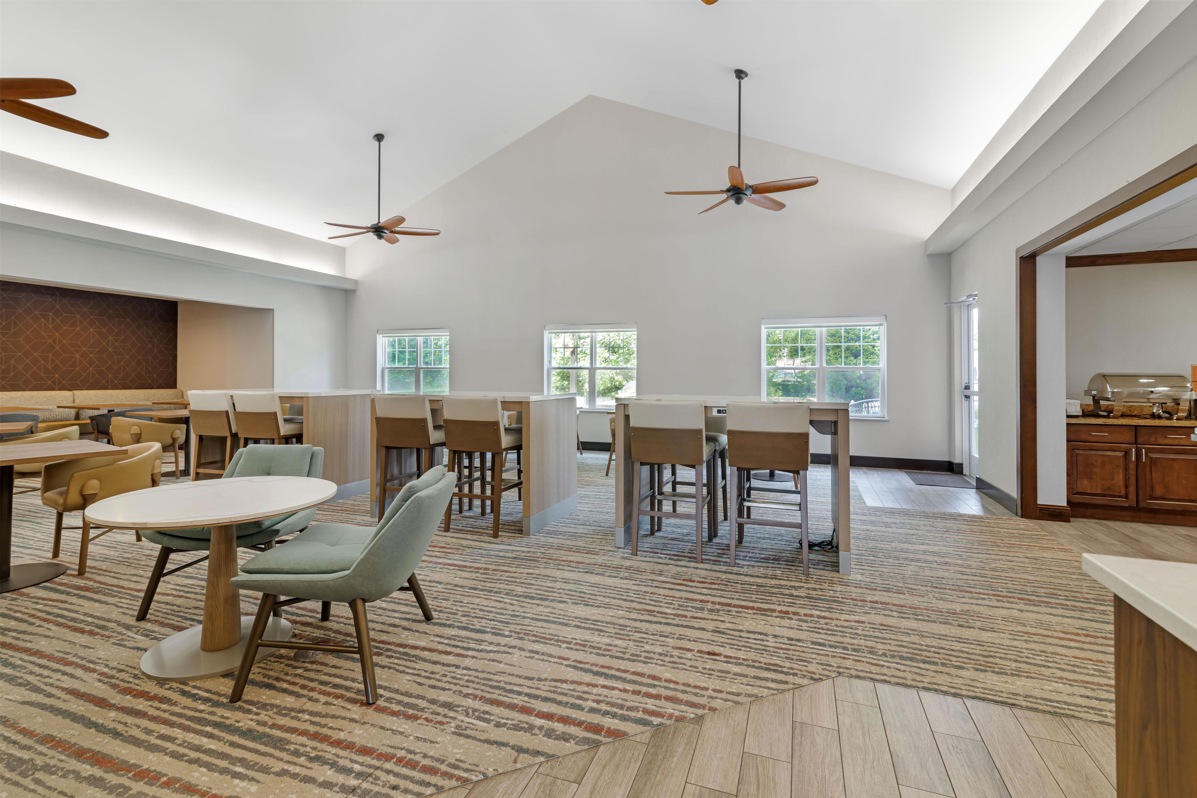 A spacious room with multiple tables and chairs, ceiling fans, and large windows.