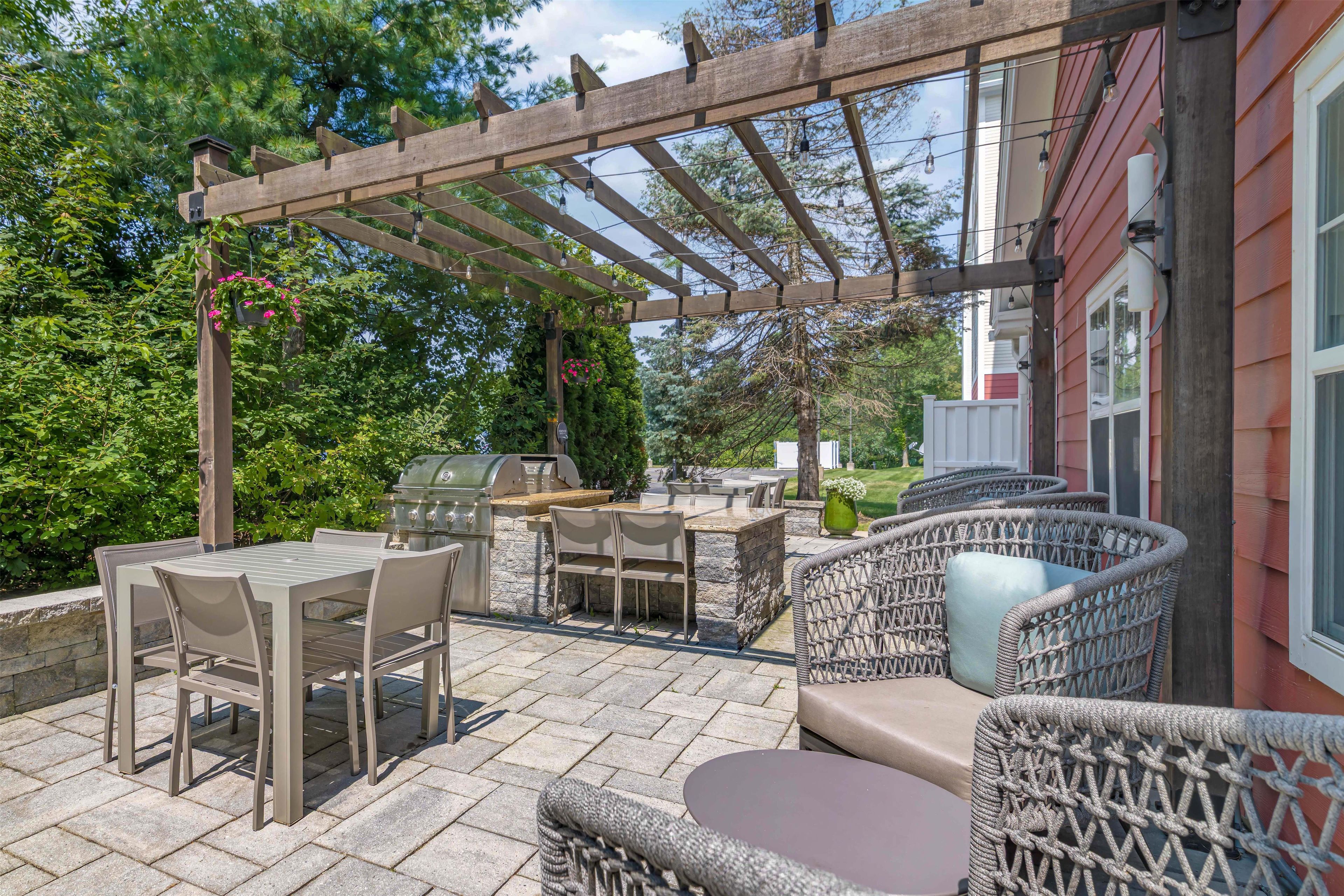Un patio exterior con una pérgola, suelo de piedra y mobiliario de exterior.