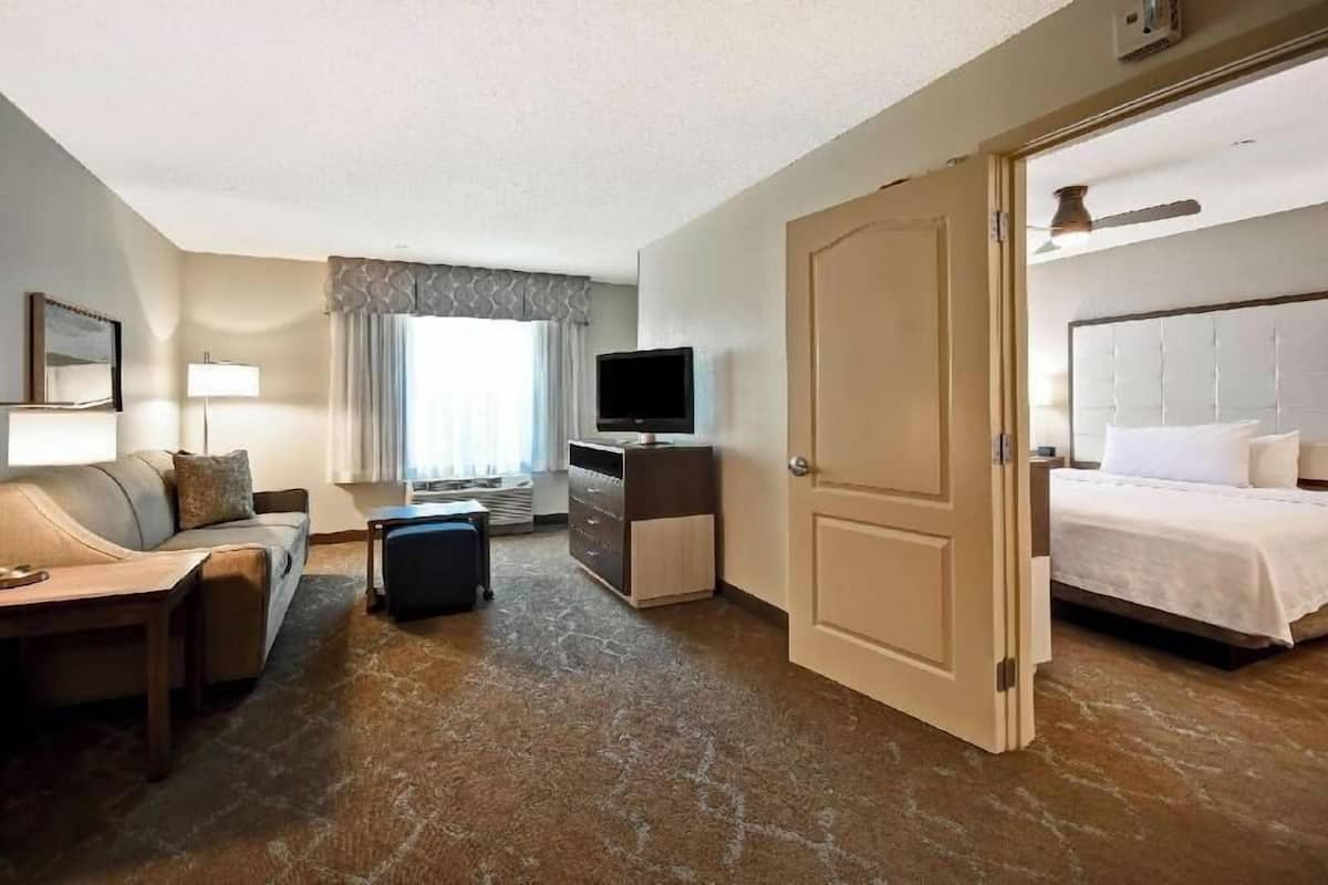 Een hotelkamer met een bed, een televisie, een bureau, een stoel, een bank en een raam met gordijnen.