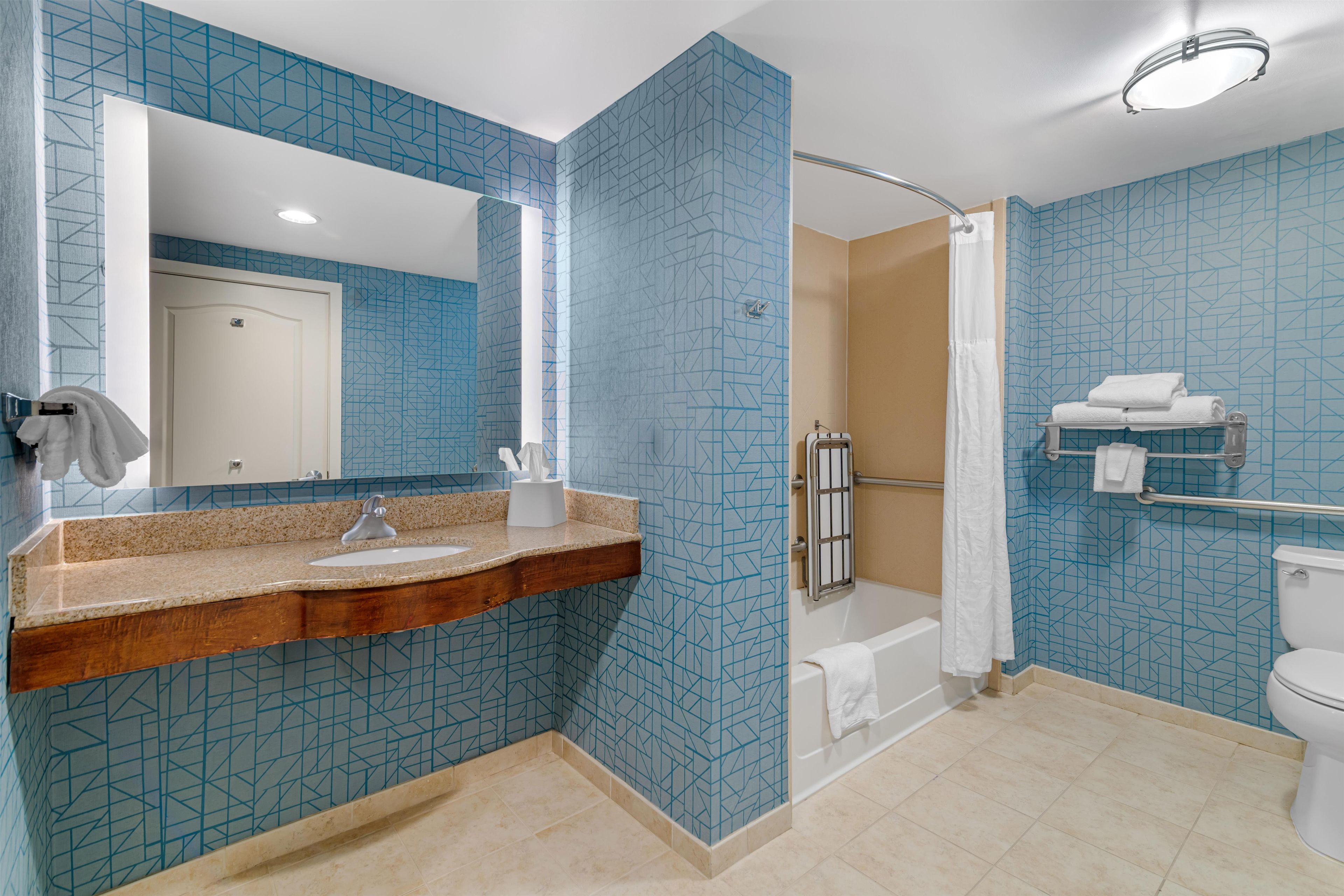 Un baño moderno con un diseño de baldosas geométricas, un mueble de tocador de madera, una bañera y un inodoro.