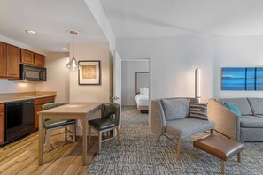 Une chambre d’hôtel moderne comprenant un coin cuisine, un espace repas, un salon avec un canapé et un tableau, ainsi qu’une chambre avec un lit et une table de chevet.