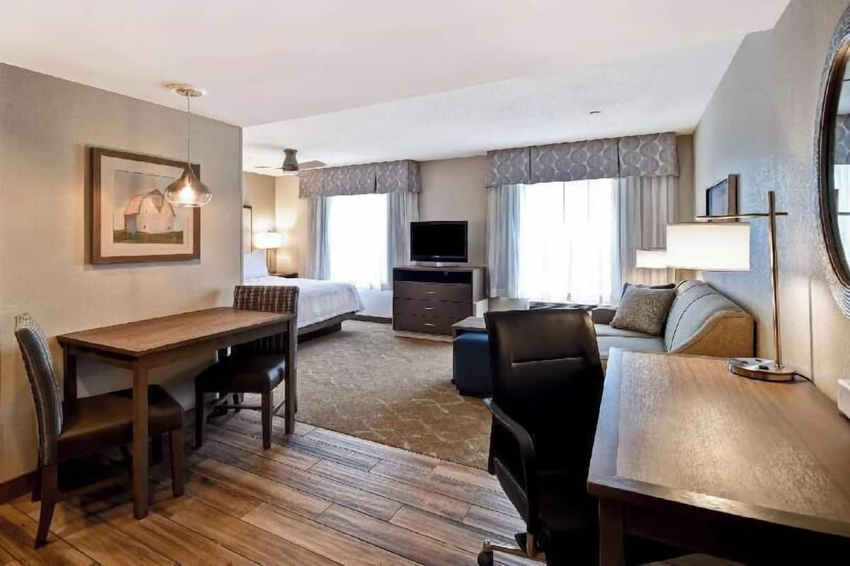 Een hotelkamer met een houten vloer, een bed, een televisie, een bureau met stoelen en een bank.
