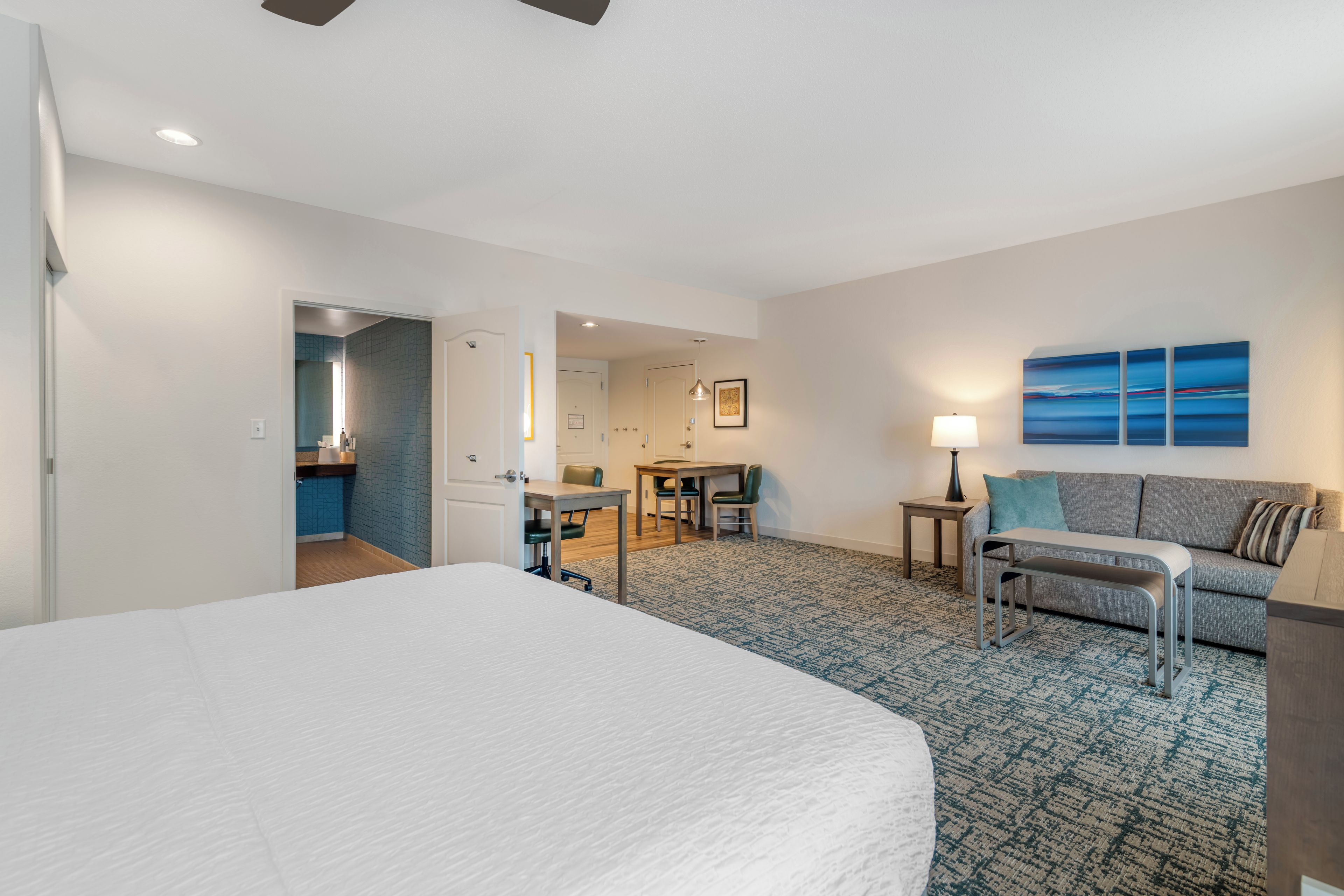 A hotel room with a large bed, a desk, a sofa, and a view of the sea.