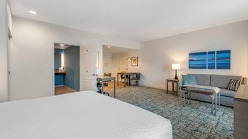 A hotel room with a large bed, a desk, a sofa, and a view of the sea.