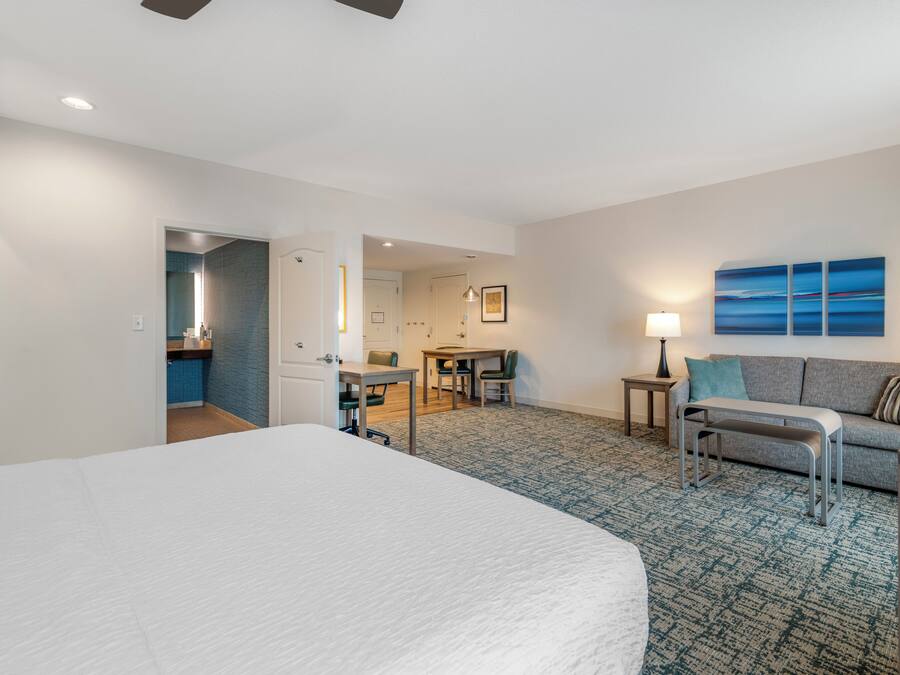A hotel room with a large bed, a desk, a sofa, and a view of the sea.