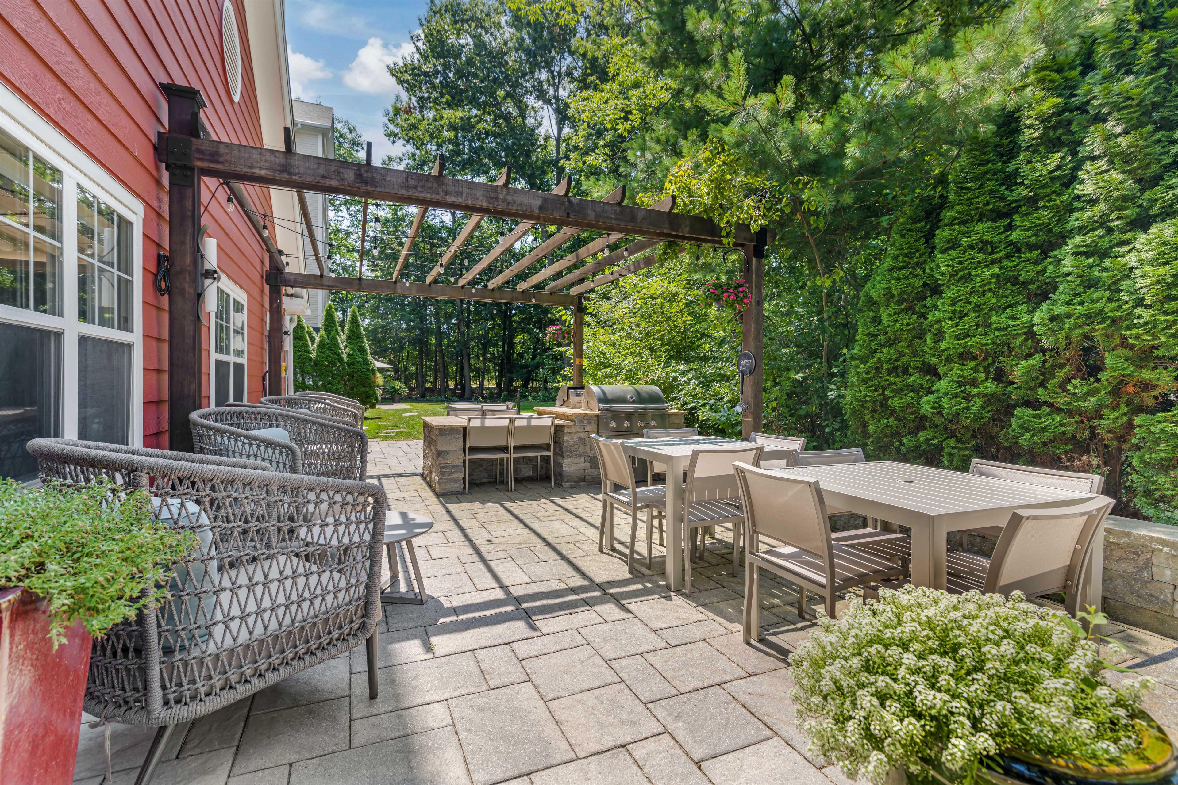 Eine Terrasse im Freien mit einer Pergola, Sitzgelegenheiten und Grillbereich.