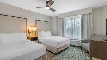 A hotel room with two beds, a desk, a chair, a ceiling fan, and a large window with curtains.
