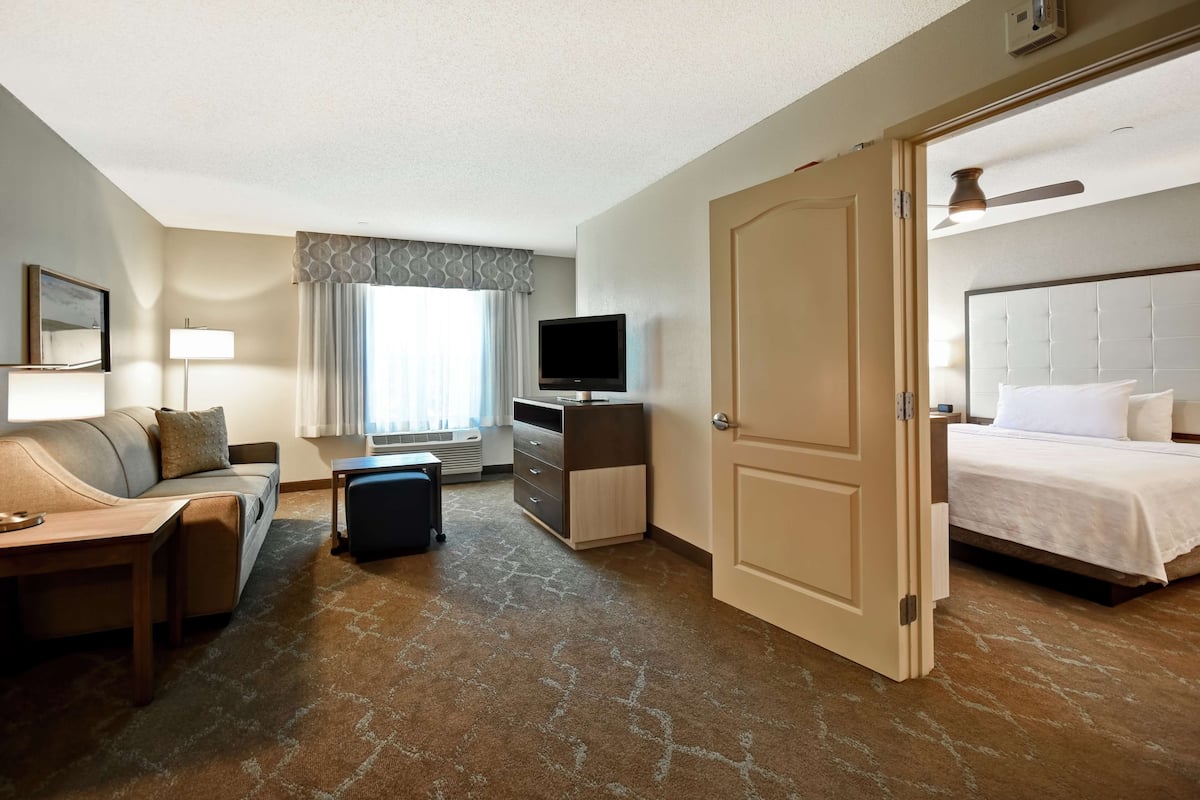 Een hotelkamer met een bed, een bank, een bureau, een televisie en een raam met gordijnen.